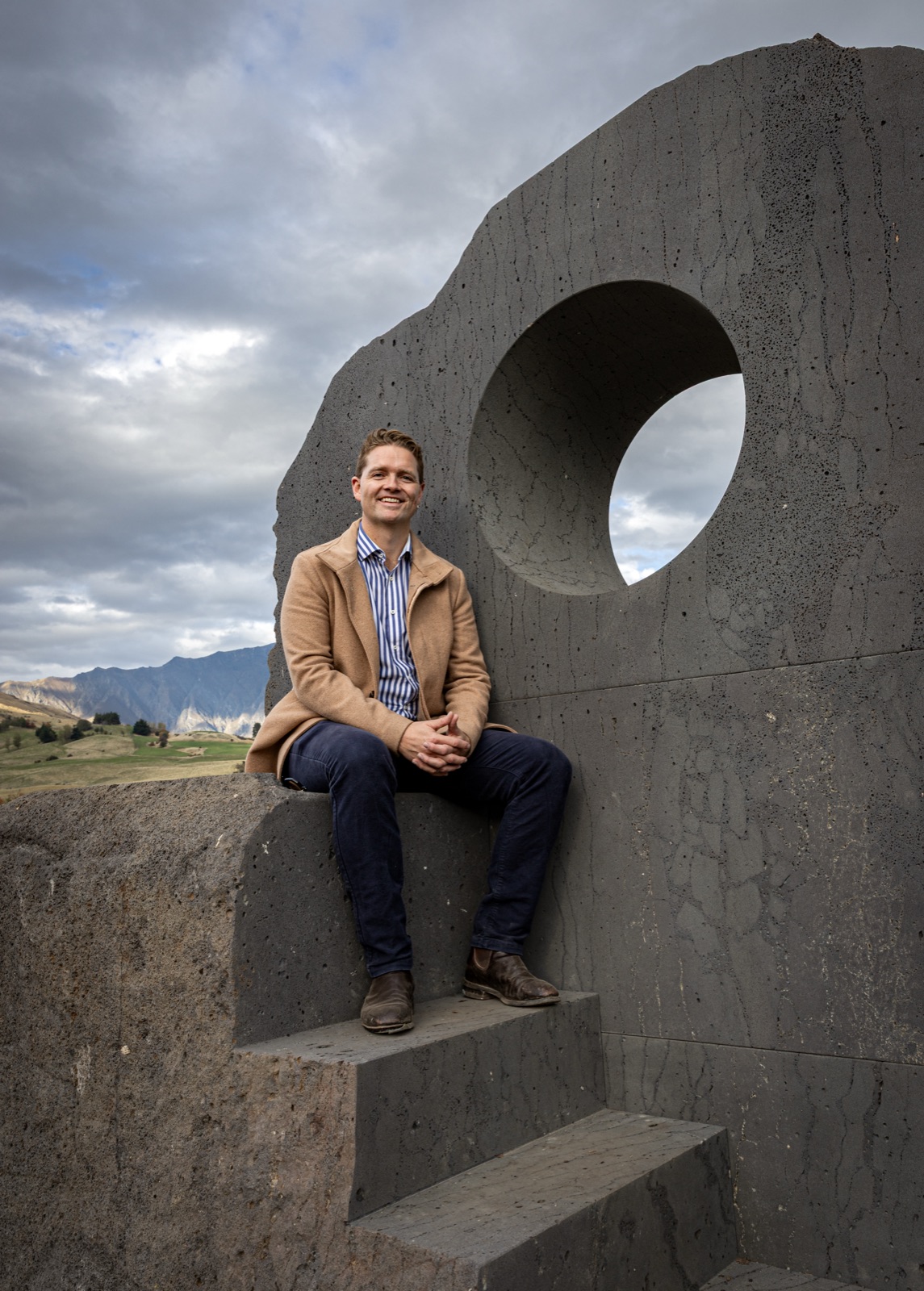 Sam Johnson sitting on Interlude, a sculptural concrete seat in Jardine Park, Queenstown