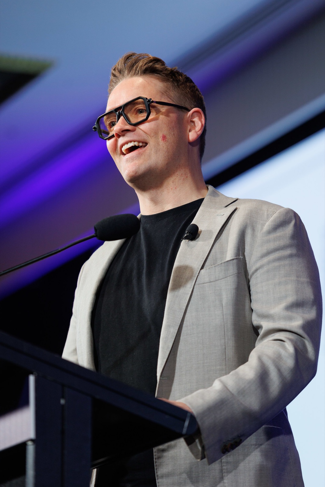 Sam Johnson laughing at the lectern on a conference stage