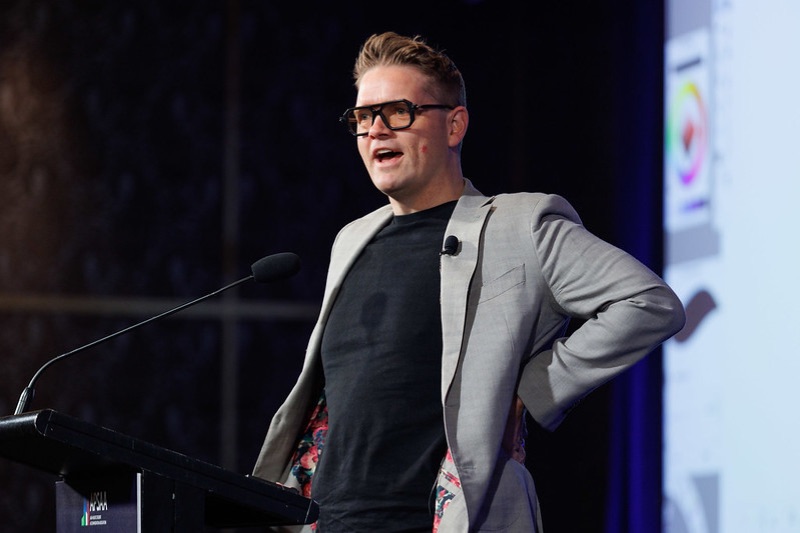 Sam speaking animatedly beside a lectern