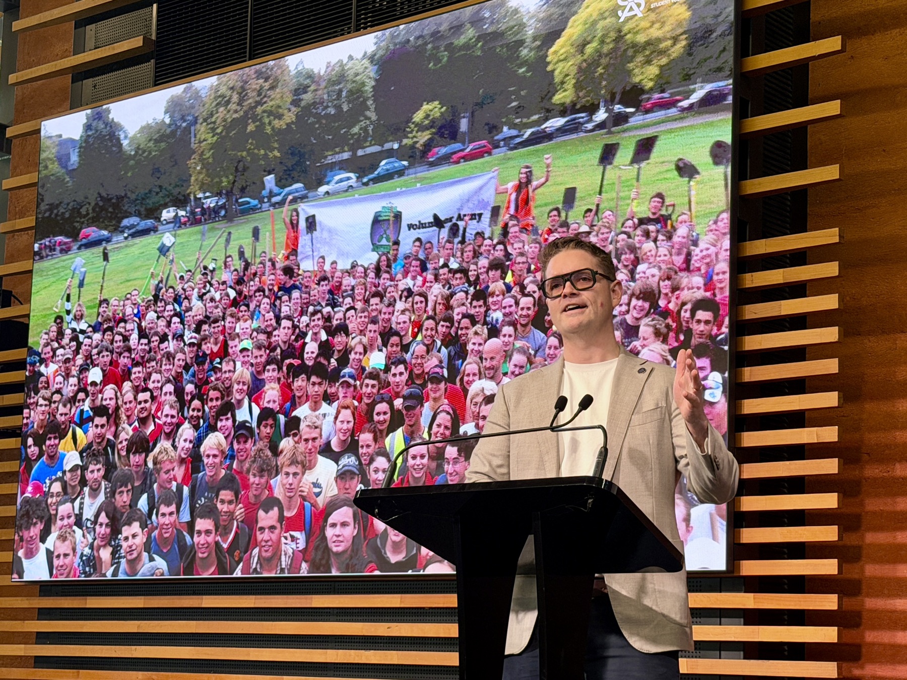 Sam presenting in front of a screen showing a crowd of volunteers