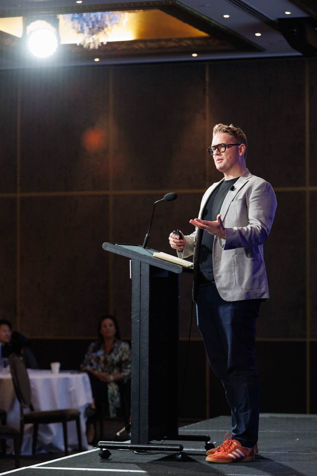Sam presenting from a lectern in a hotel ballroom with guests seated at tables